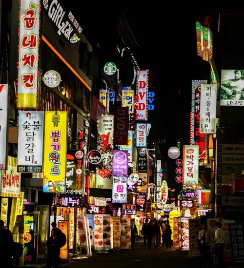 Explore Seoul's vibrant nightlife on a bustling neon-lit street lined with shops and restaurants.
