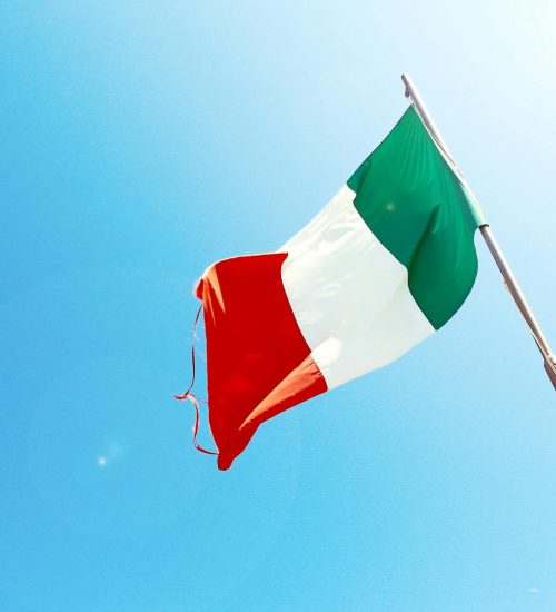 Vivid image of the Italian flag waving on a flagpole against a bright blue sky.