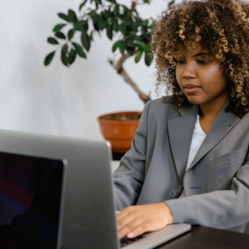 Professional woman in suit working on laptop at desk with plant.
