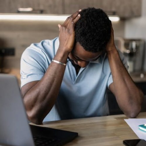 A man sits at a desk with his head in hands, experiencing stress in a home office setting.