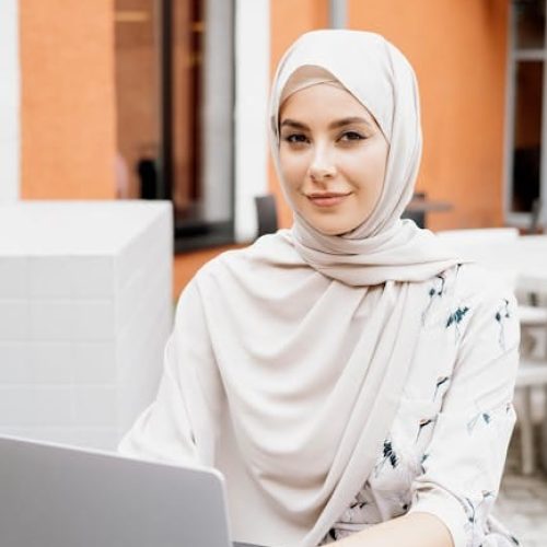 Young woman in hijab confidently working on a laptop outdoors, showcasing modern lifestyle.