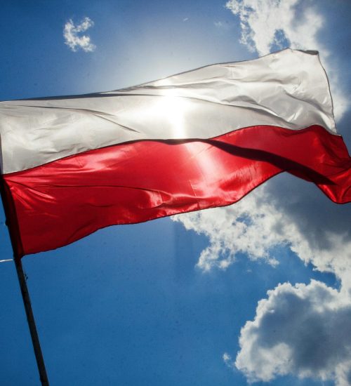 A Polish flag flutters against a bright blue sky with clouds, symbolizing national pride.